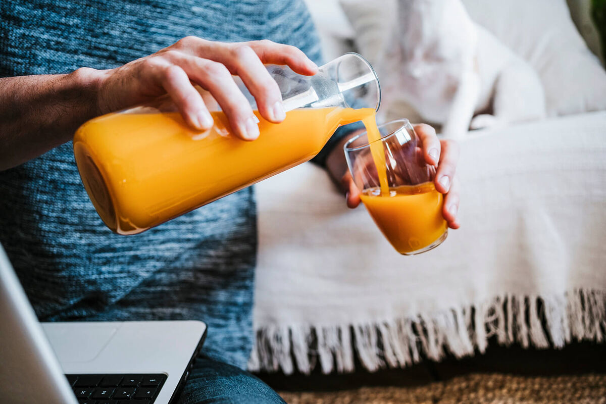 Man pouring juice in glass while sitting with laptop at home