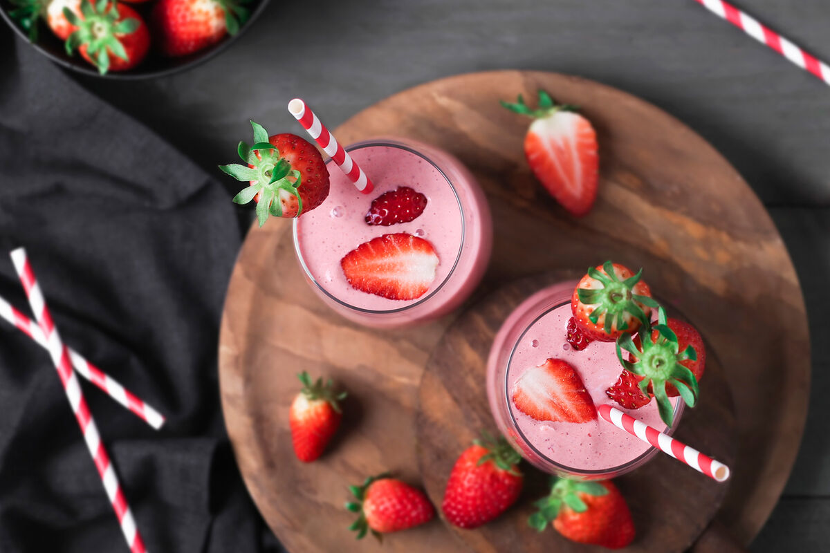 Glasses of strawberry smoothie and strawberries on dark wood