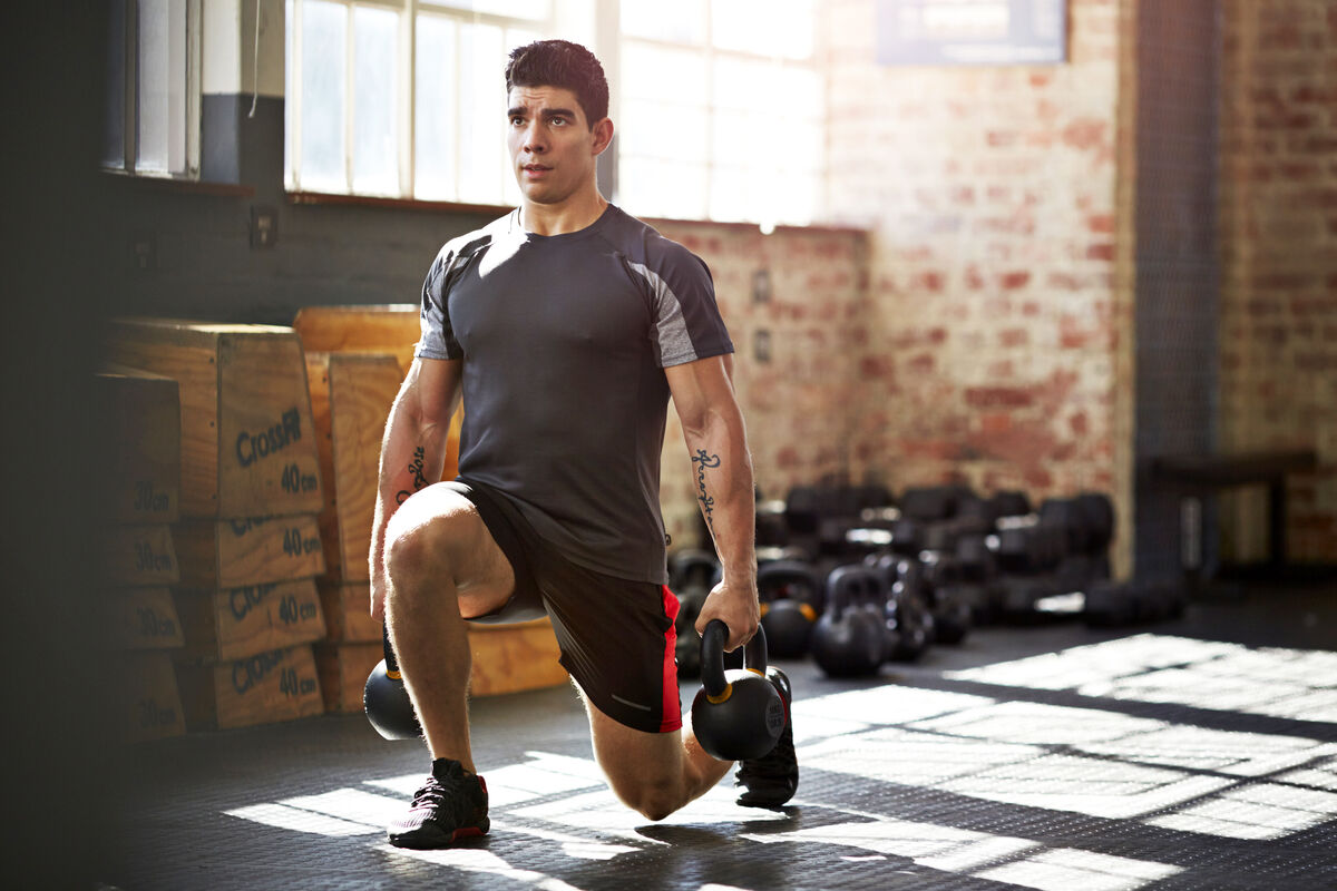 Gym instructor doing lunges with kettlebells