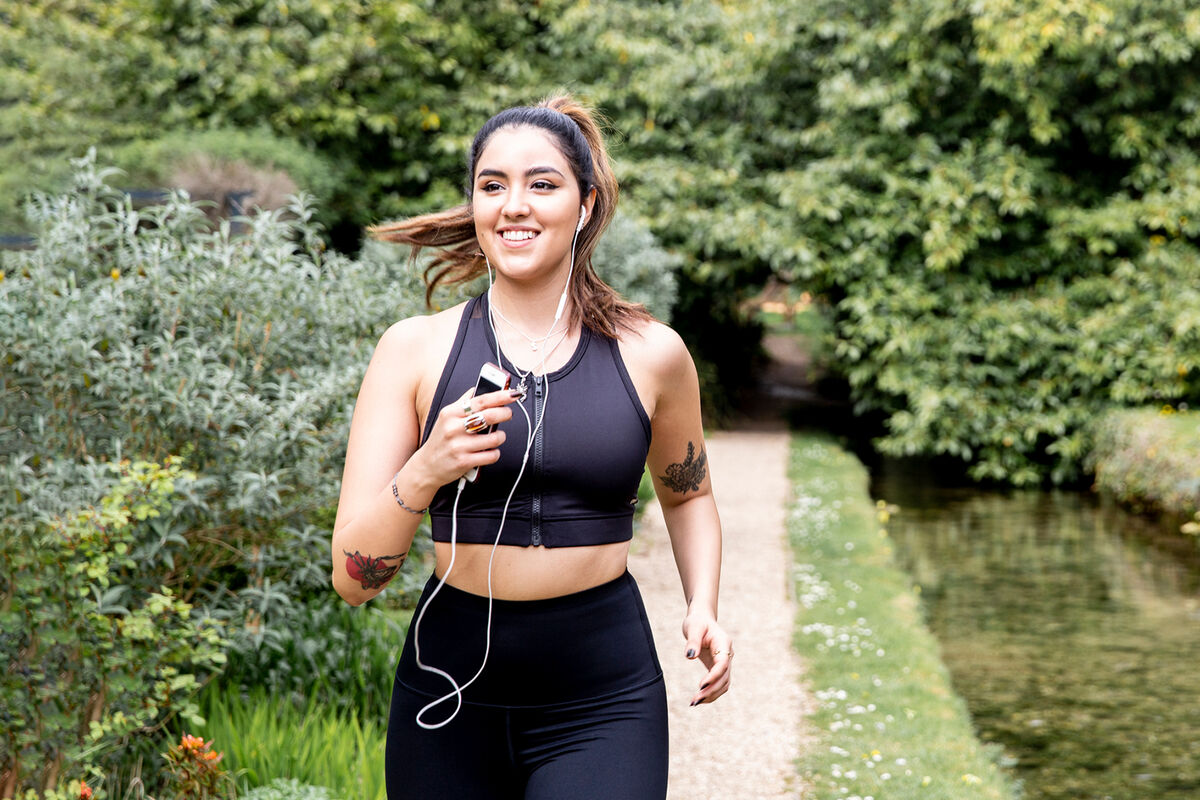 Young female runner listening to earphones while running on riverside path