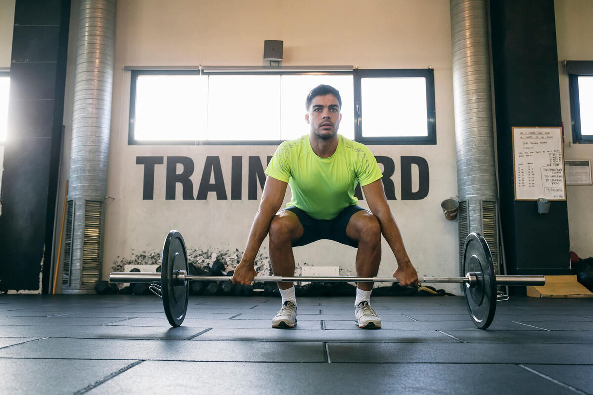 Serious male athlete lifting deadlift while standing in gym