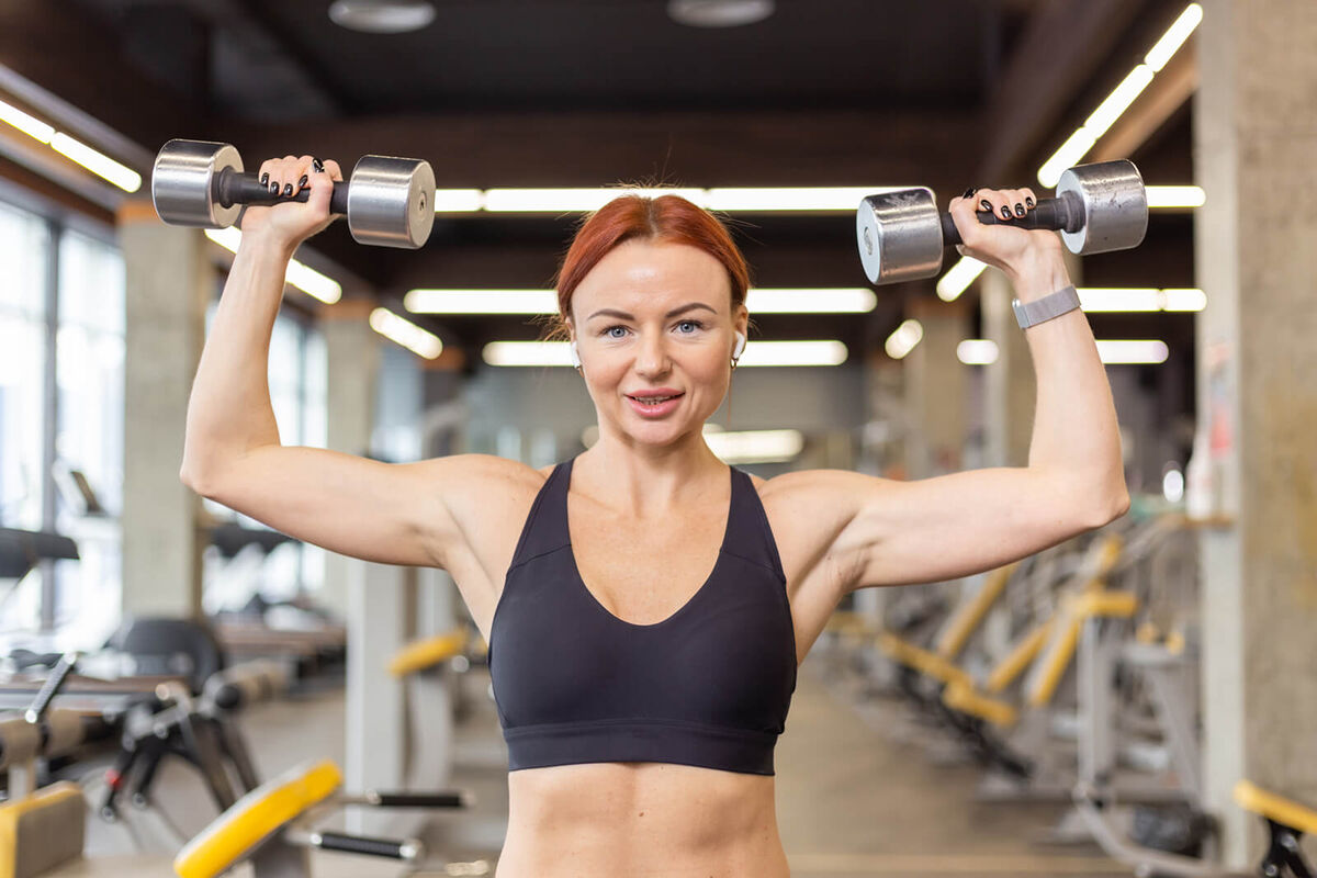 woman trains shoulder muscles doing overhead dumbbell press