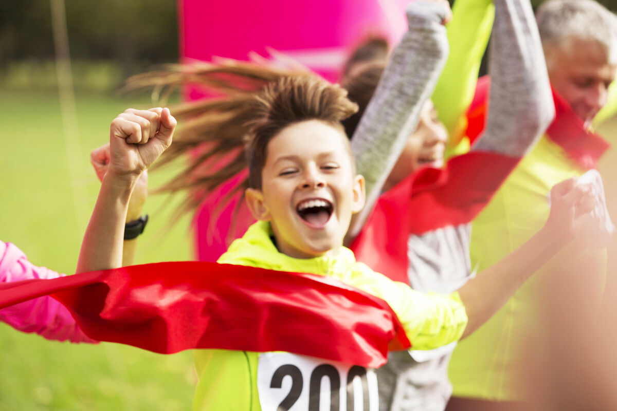 Enthusiastic boy runner crossing charity run finish line