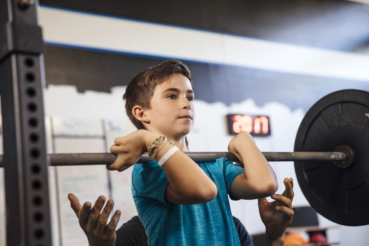 Father assisting son lifting weights in gym