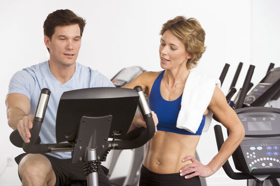 Personal trainer assisting man on stationary bike