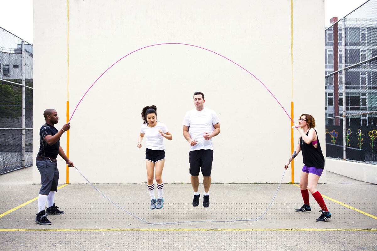 Friends playing double Dutch on street against wall