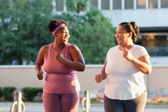 two women getting fit jogging walking in park