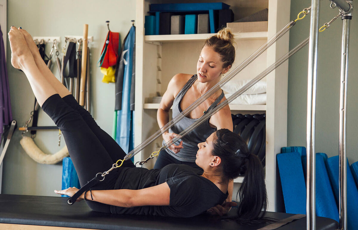Woman and personal trainer using pilates reformer