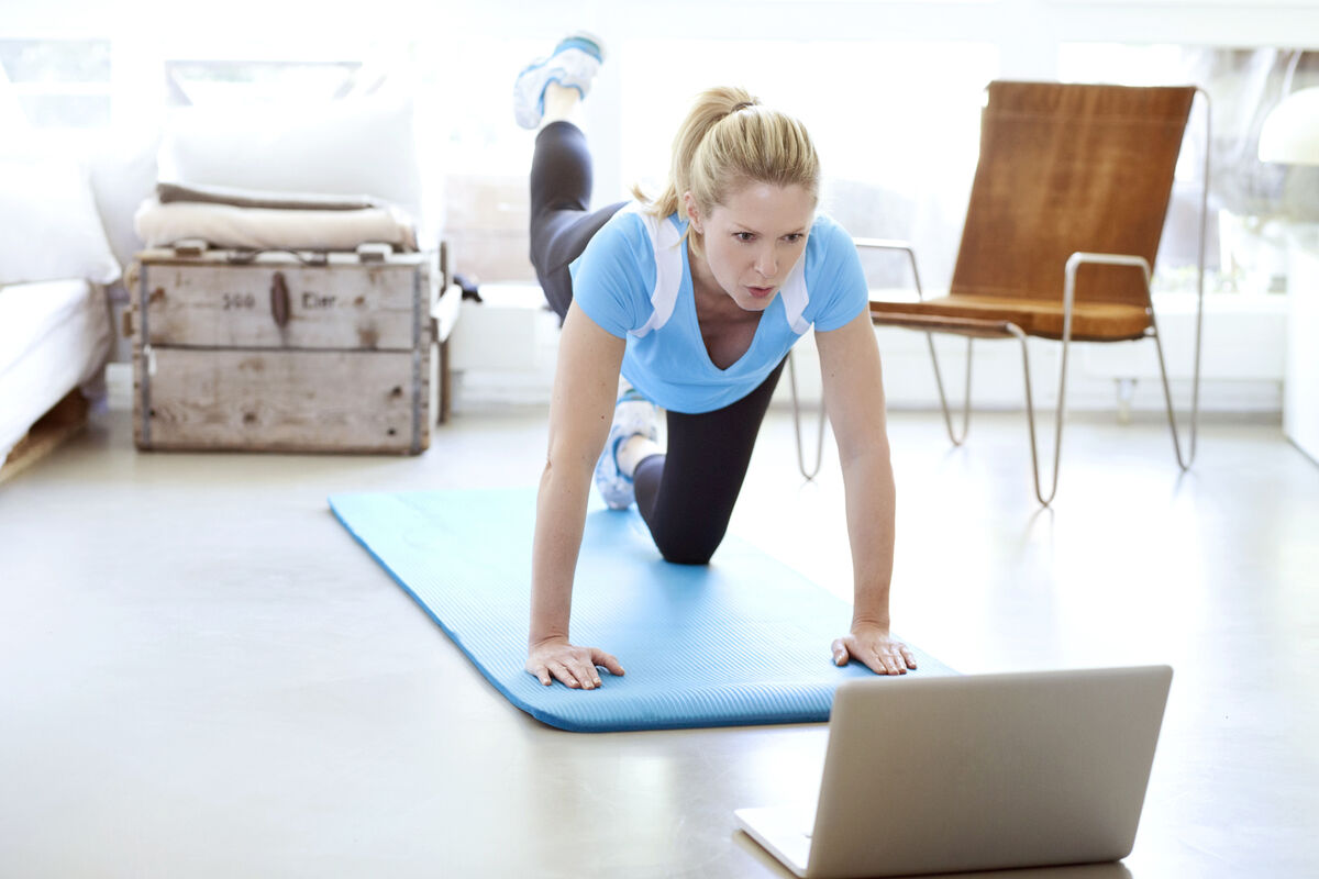 Woman looking at laptop exercising on gym mat in living room