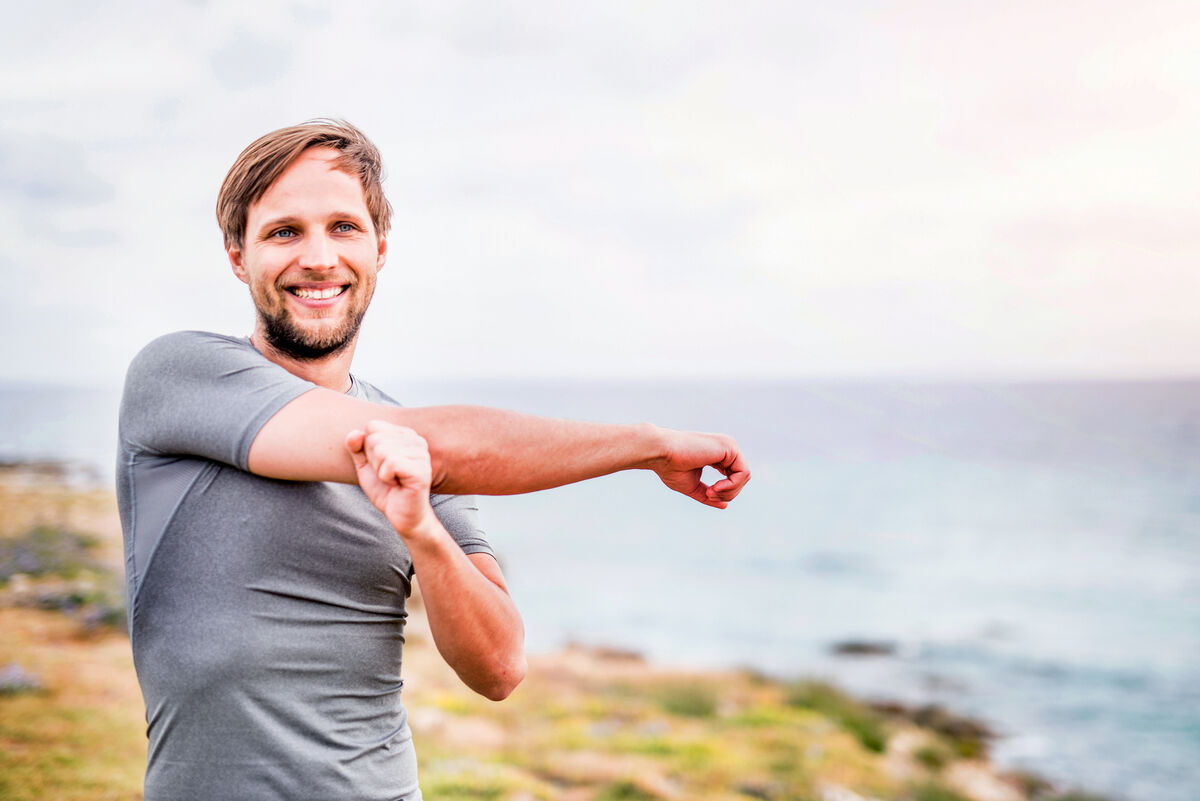 Happy sporty young man stretching on the coastline