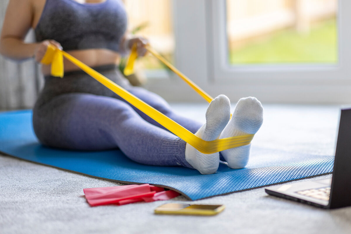 Mid adult woman practicing stretching exercise with resistance band at home