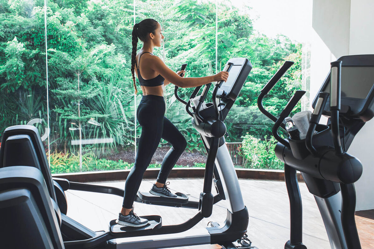 Woman training on elliptical machine in fitness club of gym