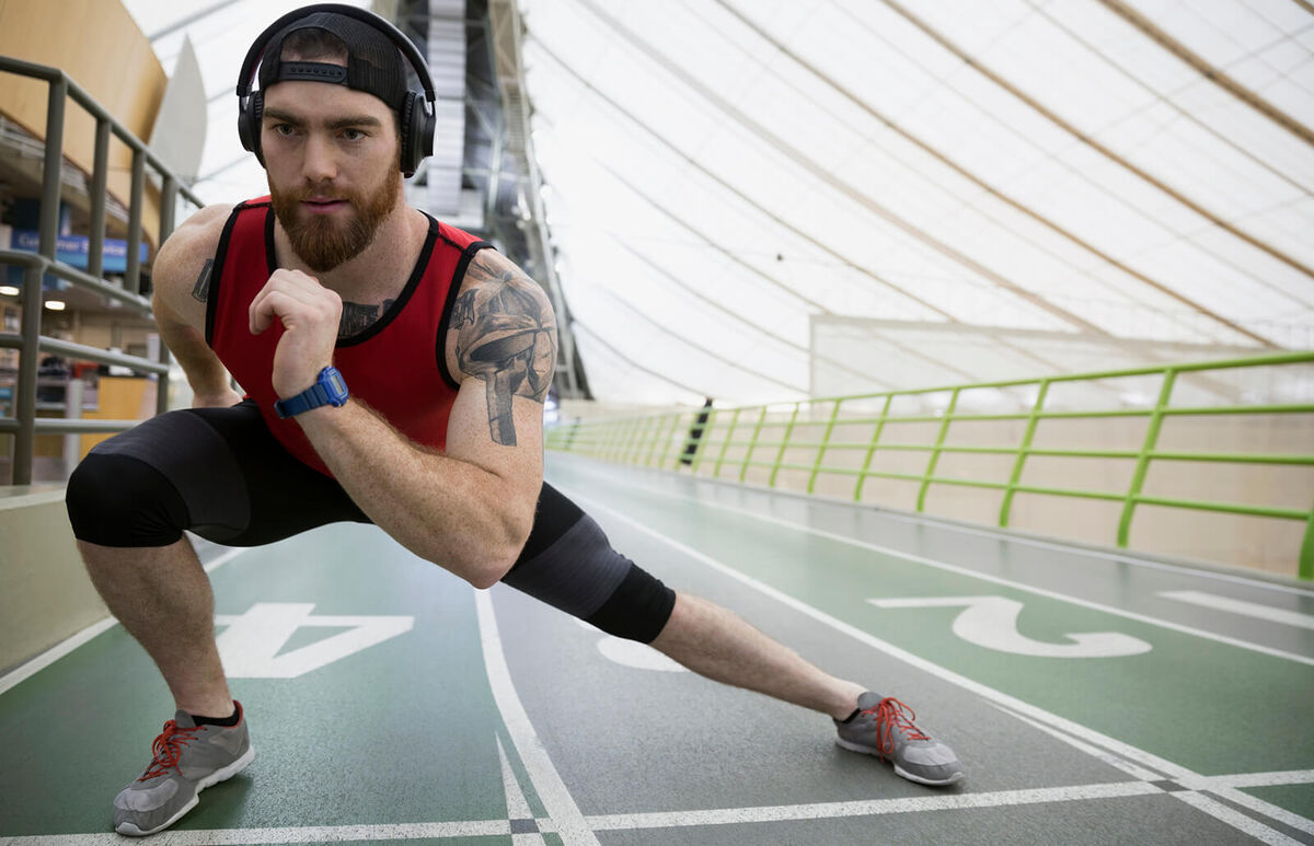Runner doing side lunge stretch on indoor track