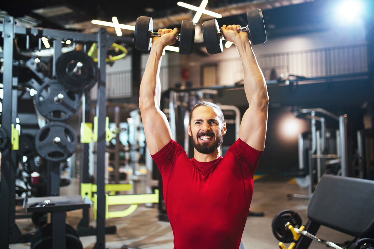 Young man lifting up dumbbells at the gym