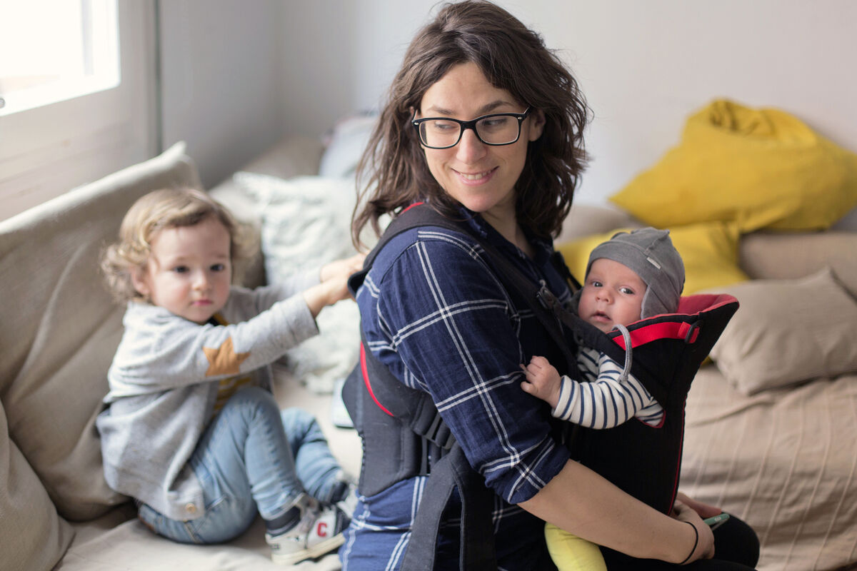 Mother is carrying newborn baby while her toddler is on her back