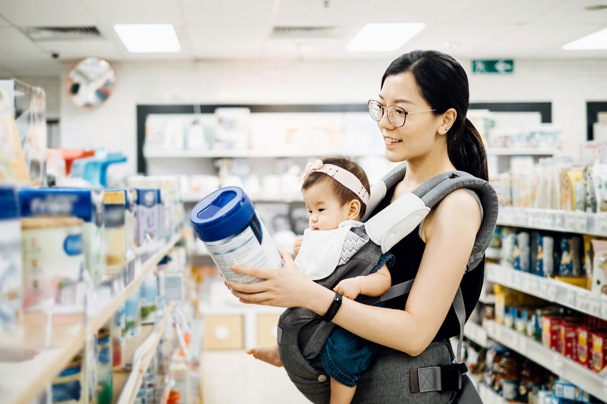 Mother carrying baby girl and looking at a variety of baby formula