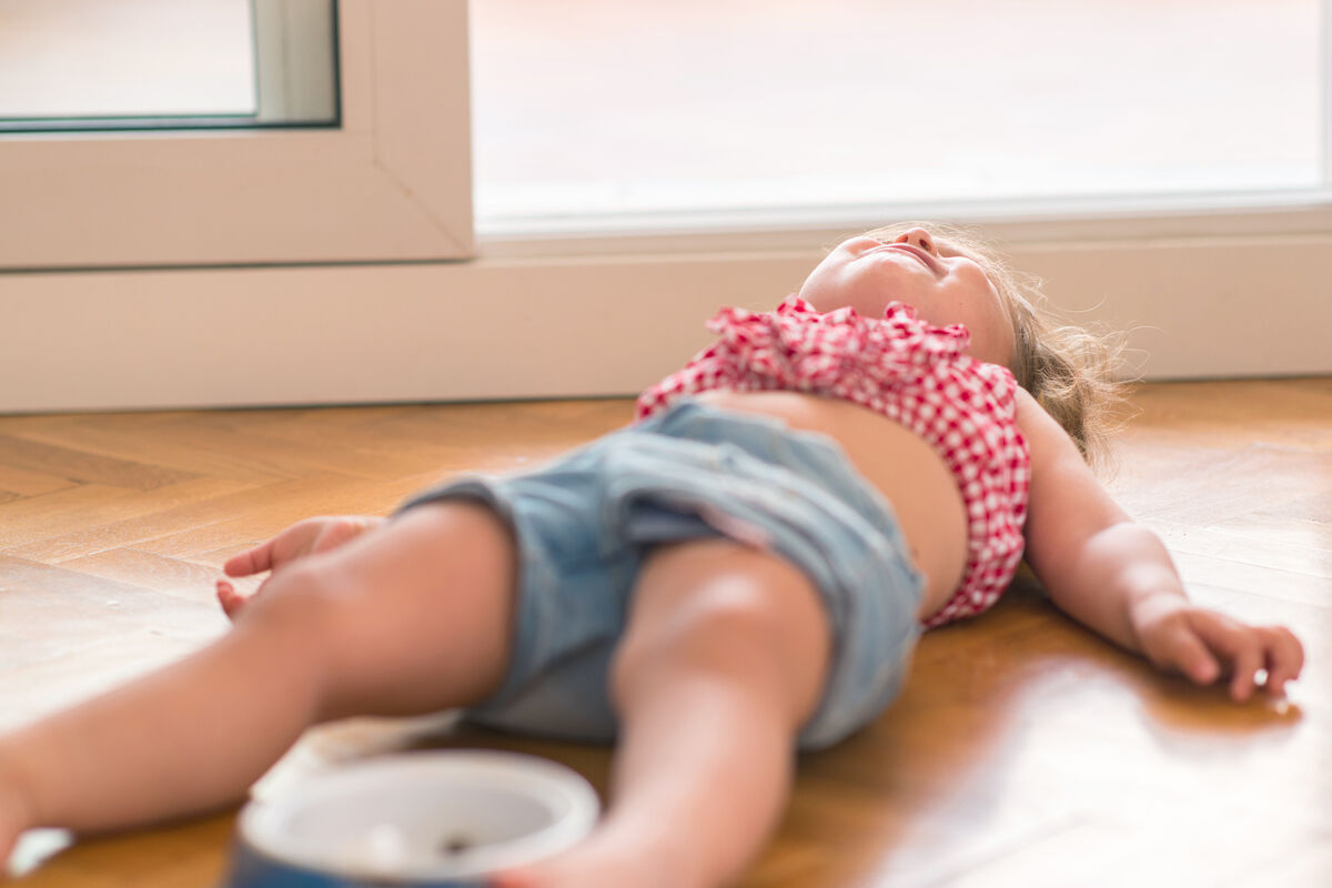 Blond child crying and shouting with tantrum laying on the floor at home