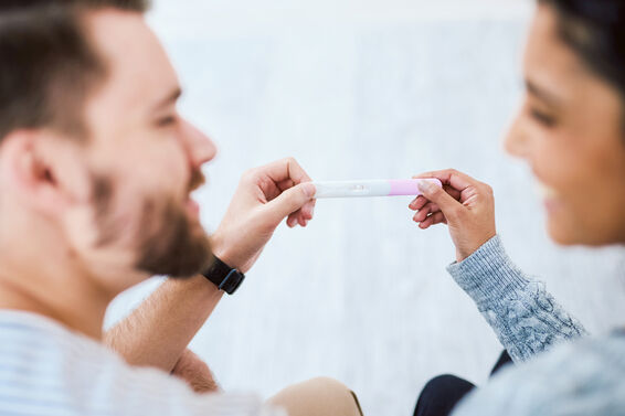 Happy young couple sitting on the sofa together and holding a positive pregnancy test