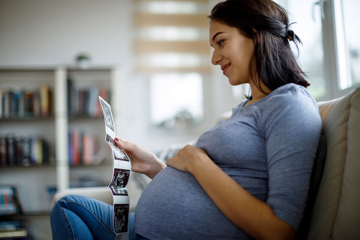 Happy pregnant woman looking at ultrasound scan at home