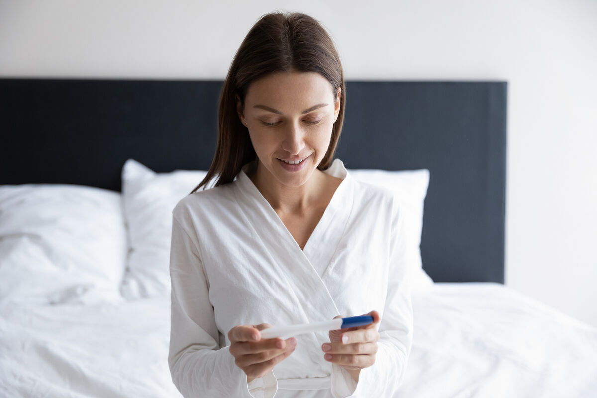 Smiling woman sitting on bed, looking at ovulation kit