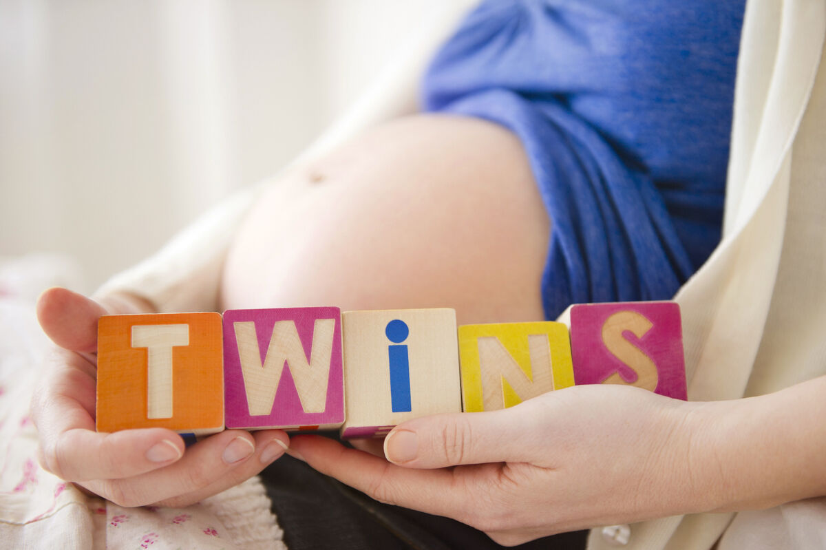 Pregnant woman holding wooden blocks saying "twins"