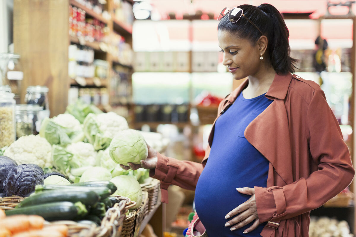 Pregnant woman shopping for cabbage in grocery store