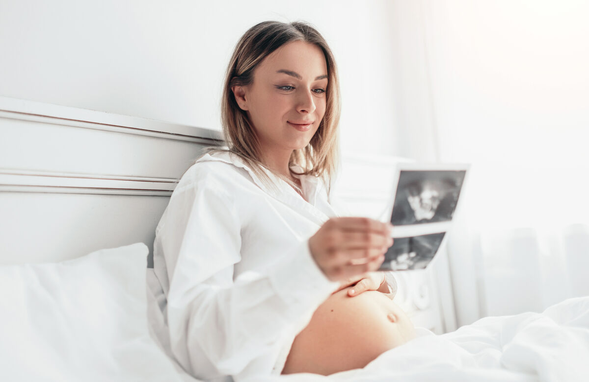 Pregnant woman smiling and looking at ultrasound scan on bed