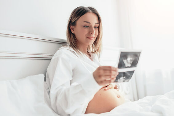 Pregnant woman smiling and looking at ultrasound scan on bed