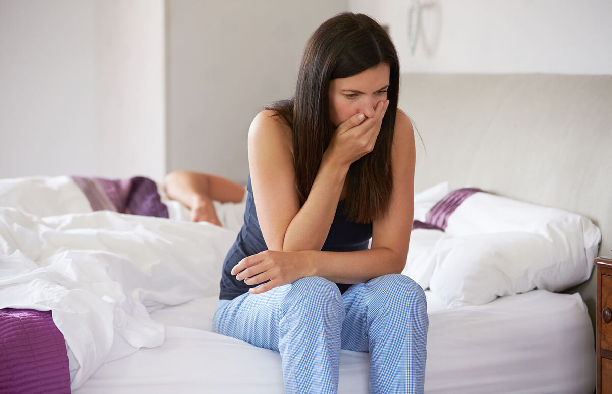 Woman sitting on bed feeling sick