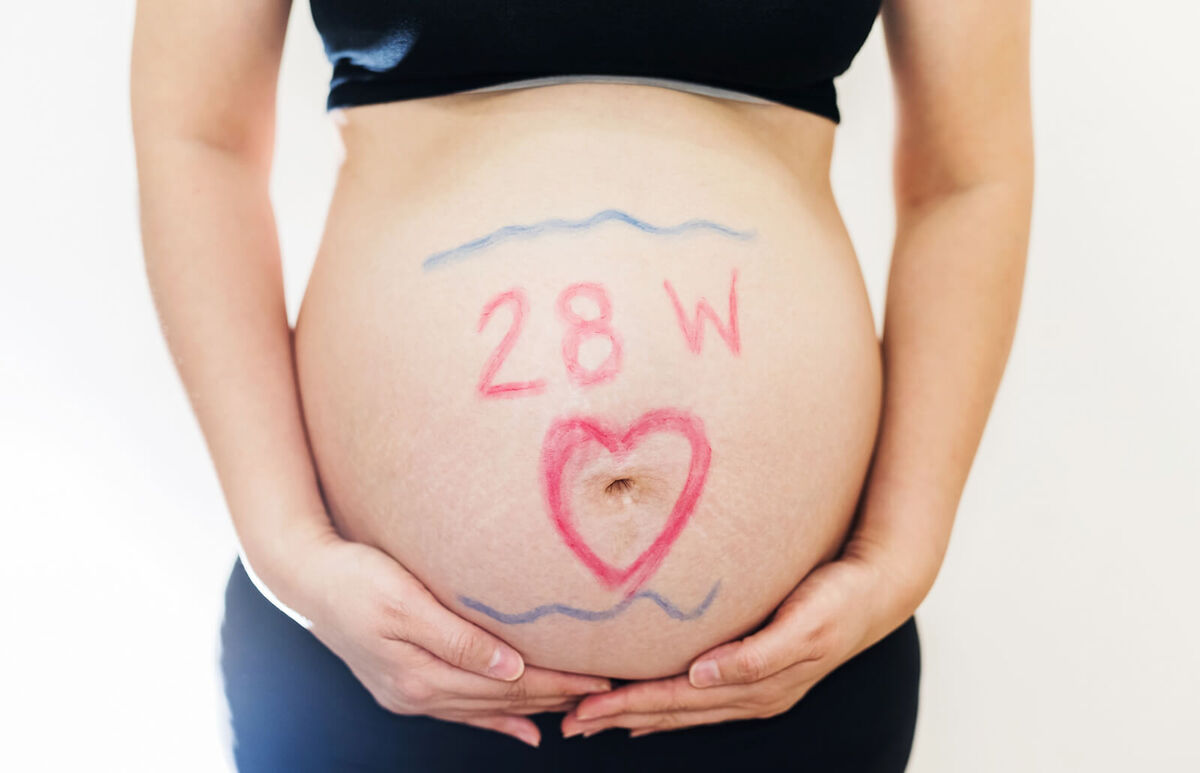 Pregnant woman measuring her belly at week 28