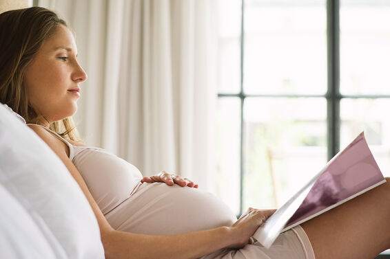 Pregnant woman reading magazine in bed