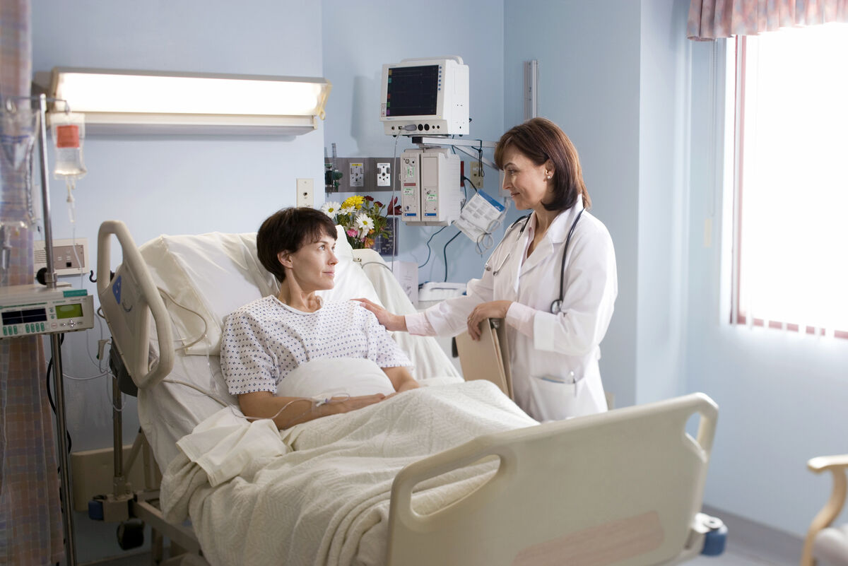Female doctor comforting female patient lying in hospital bed