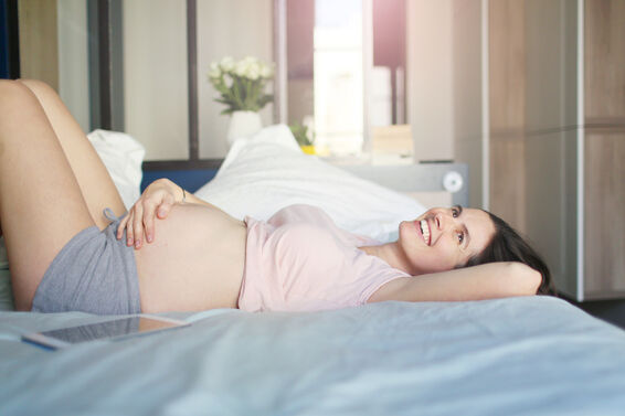 Pregnant woman smiling, laying on her bed