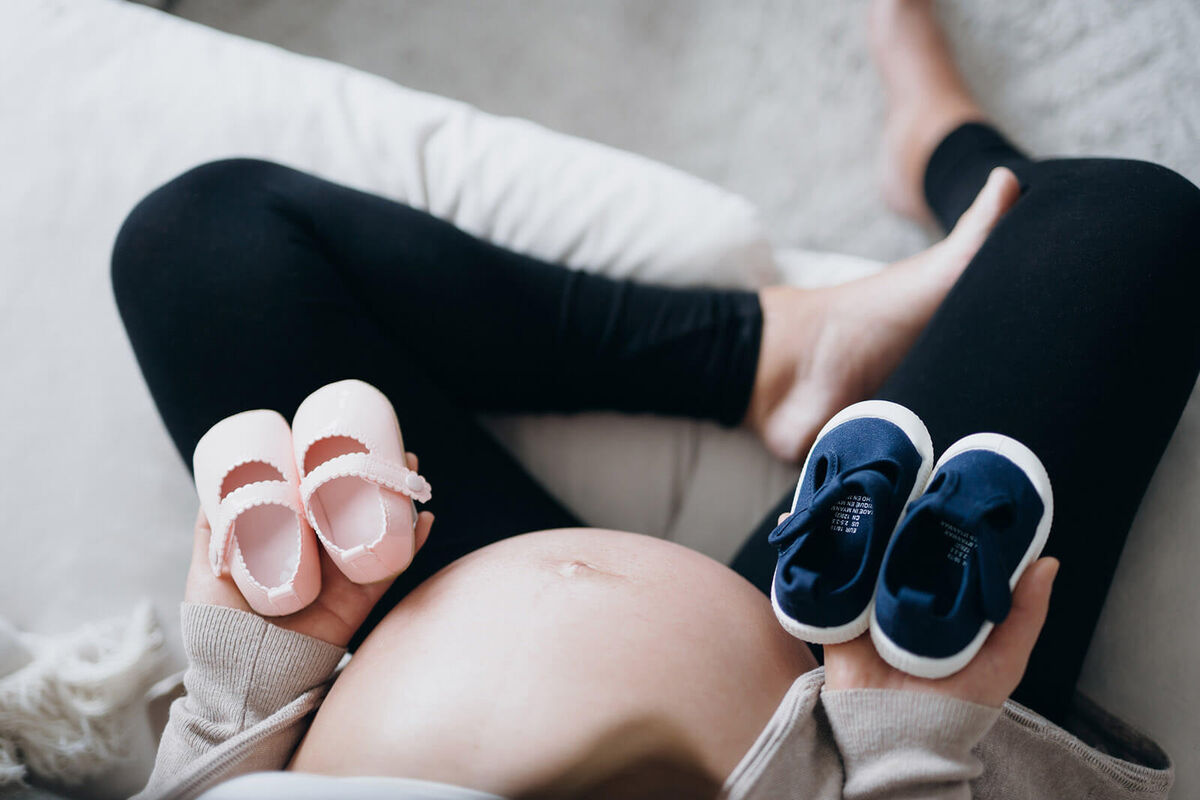 pregnant woman holding a pair of blue and pink baby shoes