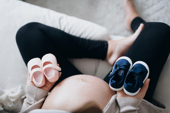 pregnant woman holding a pair of blue and pink baby shoes