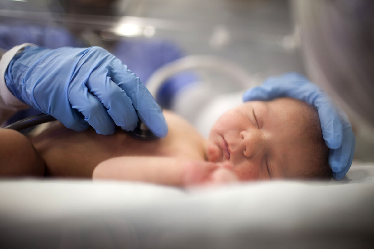 Nurse listening to heartbeat of newborn in incubator