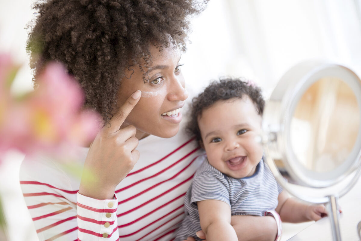 Mother holding baby son applying face cream in mirror