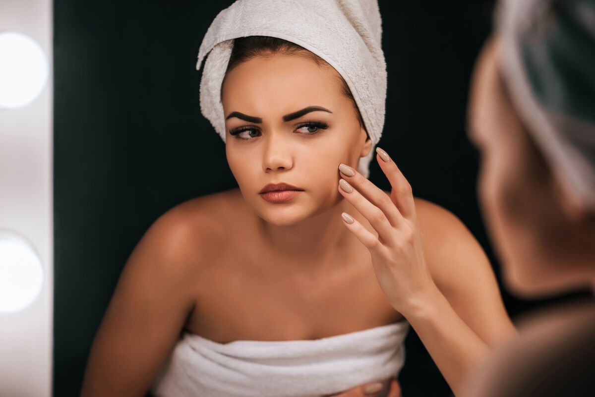 woman looking at skin in mirror