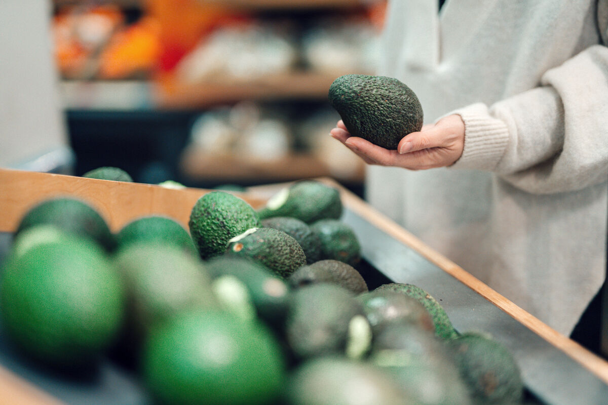 Woman Buying Avocado At Grocery Store