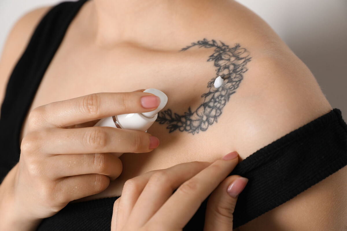 Woman applying cream onto tattoo on her skin