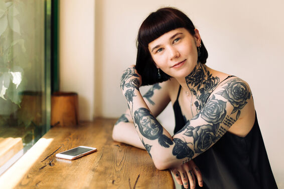woman with many tattoos and short dark hair is posing sitting at wooden bar counter