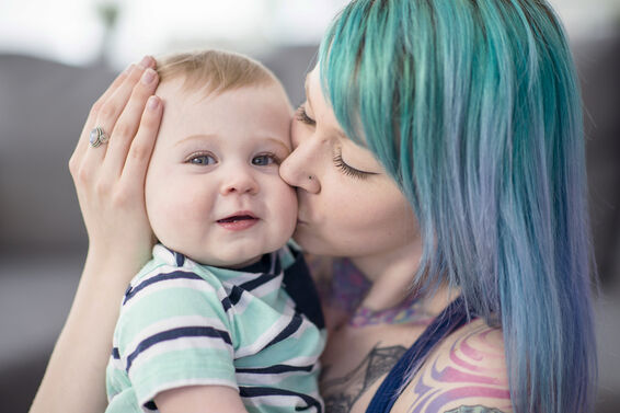 Young woman with tattoos holding and kissing baby boy