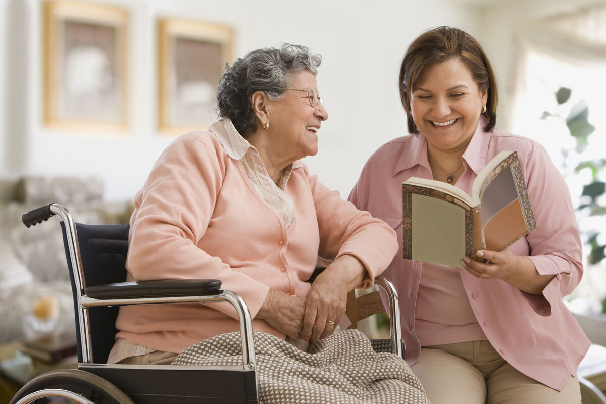 caregiver reading to elderly woman in wheelchair