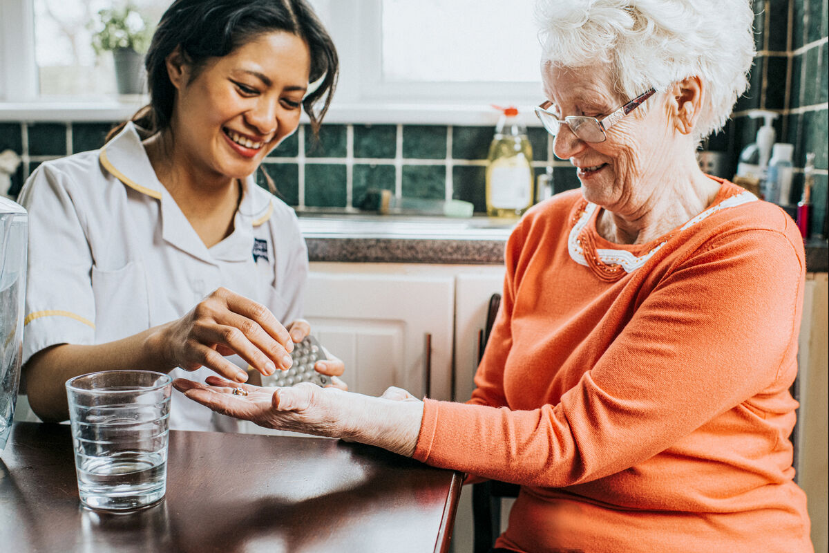 A care assistant hands an elderly woman her medication