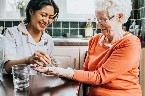 A care assistant hands an elderly woman her medication