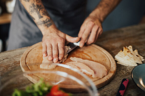 Close up of chef's hands cutting chicken meat on wooden board