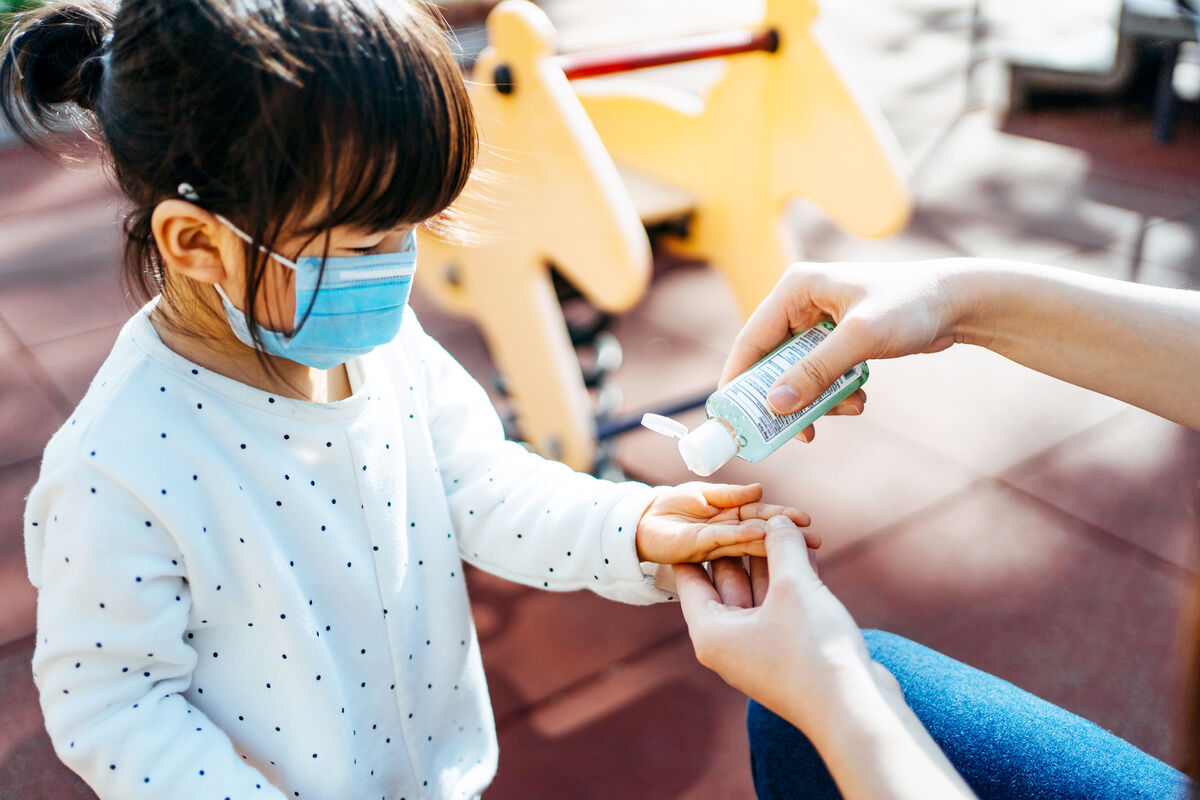 Young mother squeezing hand sanitizer onto little daughter's hand in the playground